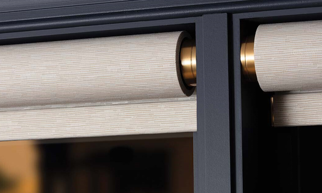 Close-up of motorized roller shades with brass hardware on black window frames