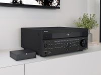 A Sony AV receiver displayed on a white cabinet alongside a compact media device and decorative plants.